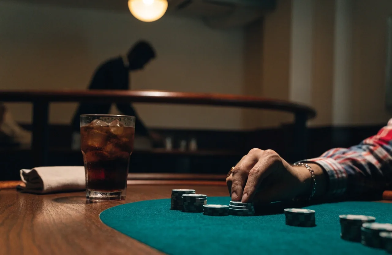 Okraj hracího stolu s hromádkou žetonů pod teplým světlem v pokerové herně
